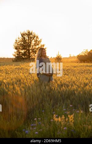 Eine schwangere Frau in einem rosa Kleid geht in der Natur. Die werdende Mutter genießt die Schwangerschaft. Stockfoto