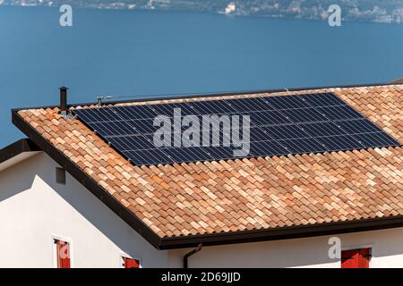 Sonnenkollektoren auf dem Dach eines Hauses mit einem blauen See im Hintergrund. Konzept für erneuerbare Energien Stockfoto