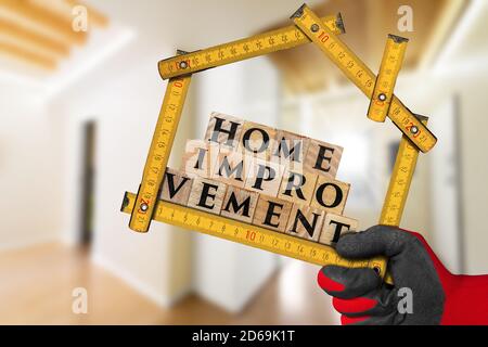 Hand mit Arbeit Handschuh mit einem hölzernen Klapplineal in Form von Haus mit Text Home Improvement, aus Holzblöcken. Stockfoto