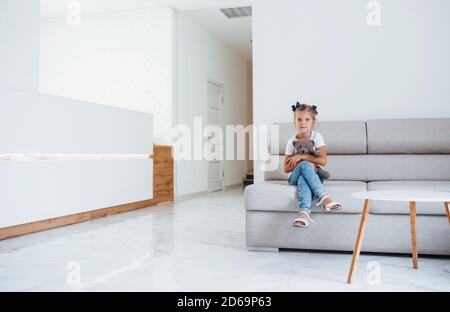 Nettes kleines Mädchen mit Teddybär in den Händen sitzt in Warteraum des Krankenhauses Stockfoto