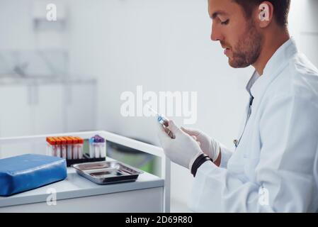 Männlicher Arzt mit Spritze bereitet sich auf die Blutentnahme vor Im Klinikraum Stockfoto