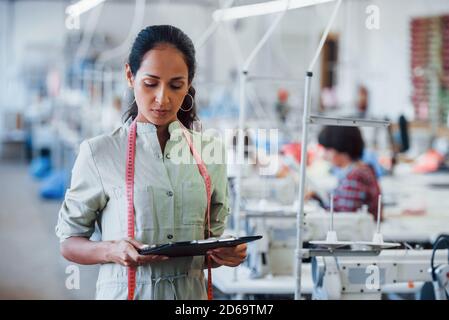 Brunette Schneiderei arbeitet in der Fabrik und hält Notepad in Hände Stockfoto