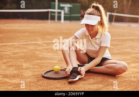 Sitzt auf dem Boden. Junge Tennisspielerin in sportlicher Kleidung ist auf dem Platz im Freien Stockfoto