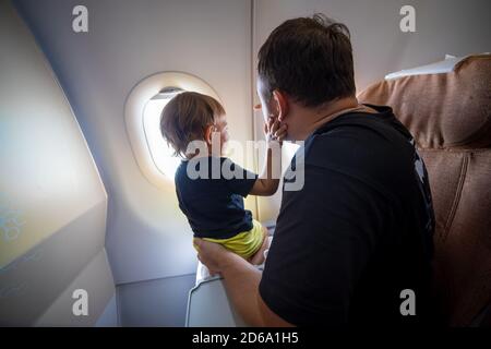 Vater und niedliche Kleinkind sitzen auf einem Flugzeug und Blick in den Himmel durch das Bullauge. First Flight Konzept, Reisen mit Kindern Stockfoto