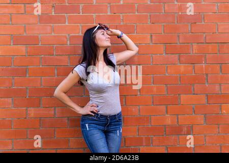 Junge schlanke Frau mit Brille, die gegen einen Ziegelstein schaut Wandhintergrund Stockfoto