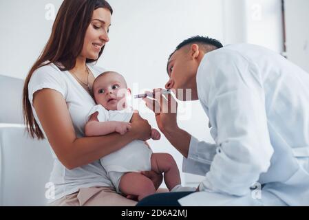 Mit der Hilfe der Mutter. Der junge Kinderarzt ist mit dem kleinen Baby tagsüber in der Klinik Stockfoto