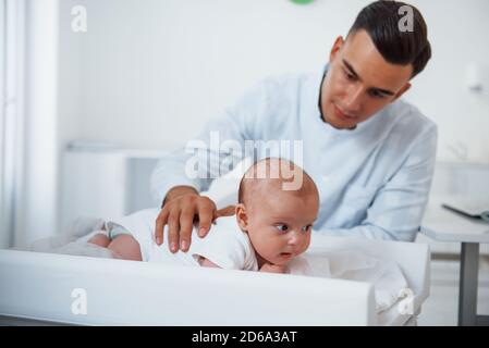 Kleines Baby liegt auf dem Tisch. Der junge Kinderarzt ist tagsüber in der Klinik Stockfoto