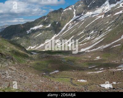 Blick auf das Bergtal mit gewundenem Quellbach und schneebedeckten Gipfeln am Stubaier Wanderweg, Stubaier Hohenweg, Sommer felsige Alpenlandschaft Stockfoto