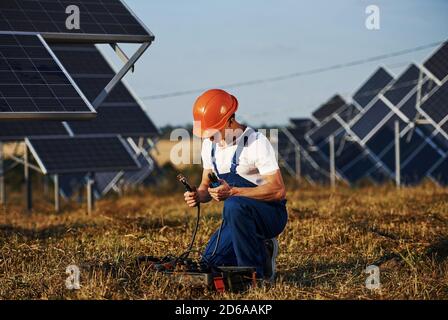 Verwendung von Sonderausrüstung. Männlicher Arbeiter in blauer Uniform im Freien mit Solarbatterien an sonnigen Tagen Stockfoto