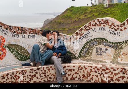 Miraflores, Peru - 4. Dezember 2008: Parque del Amor, Love Park. Junge küssende Paar auf kunstvollen Mosaikbank mit Meer und grünen Klippe im Hintergrund. Stockfoto