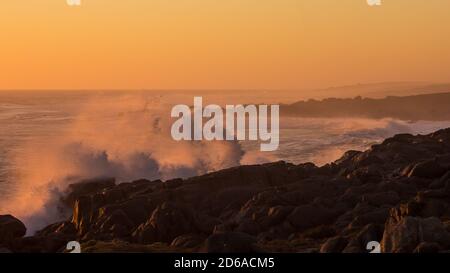 Wellen brechen mit einem Spray entlang der Rocky West Coast von Südafrika, während Sonnenuntergang Färbung alles eine rosa orange Farbe Stockfoto