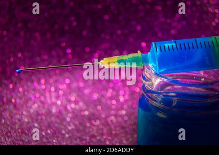 Nahaufnahme Foto von Spritze auf Flaschenhals von Blue Liquid Mit einer Nadel mit einem blauen Tropfen auf Purple Bokeh Hintergrund Stockfoto