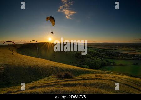 Gleitschirme fliegen bei Sonnenuntergang über Fulking Village im South Downs National Park. Brighton, East Sussex. Vereinigtes Königreich Stockfoto