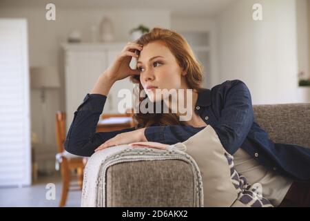 Nachdenkliche Frau, die zu Hause auf der Couch sitzt Stockfoto