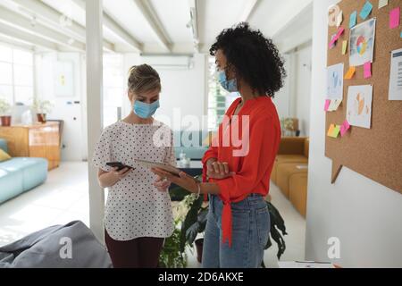 Zwei Frauen mit Gesichtsmasken diskutieren über ein digitales Tablet Im Büro Stockfoto
