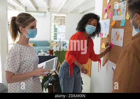 Bürokollegen mit Gesichtsmaske diskutieren über Memonotizen bei Büro Stockfoto