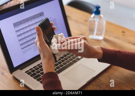 Mittelteil einer Frau, die ihr Smartphone mit einem Gewebe abwischt Stockfoto