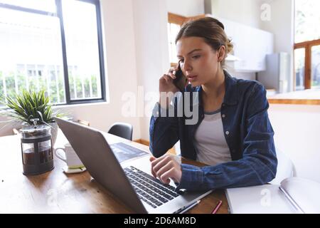 Frau spricht auf dem Smartphone, während sie mit dem Laptop zu Hause sitzt Stockfoto