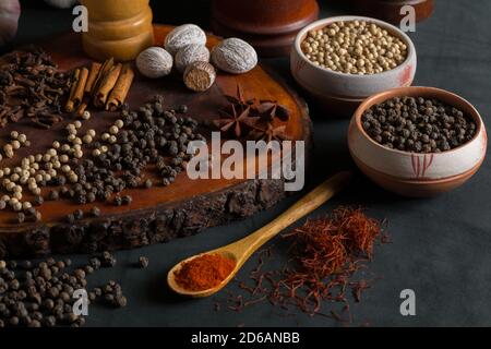 Stillleben mit verschiedenen Gewürzen wie Pfeffer, Muskatnuss, Zimt und Paprika auf schwarzem Hintergrund. Stockfoto