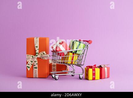Nahaufnahme eines Trolleys voll von bunten Geschenkboxen im lila Hintergrund, Weihnachtseinkäufe Stockfoto