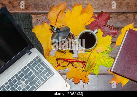 Heißer Kaffee in roter Tasse mit Dampf und Brillen auf gestapelten Büchern mit Laptop auf Holzhintergrund, Kaffeepause-Konzept Stockfoto