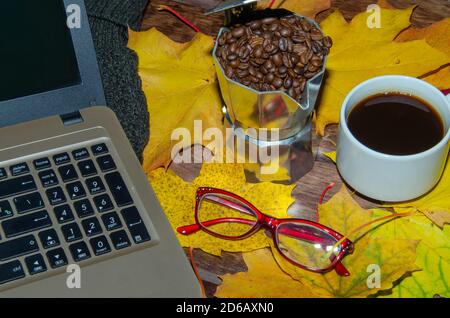 Heißer Kaffee in roter Tasse mit Dampf und Brillen auf gestapelten Büchern mit Laptop auf Holzhintergrund, Kaffeepause-Konzept Stockfoto