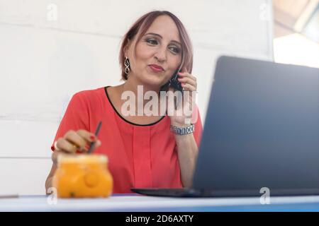 Frau, die auf einem modernen Laptop im Freien arbeitet - trendige Frau, die ruft Beim Trinken von gesundem Orangensaft - Freiberufler oder Unternehmerin Zusammenarbeit mit ihm Stockfoto