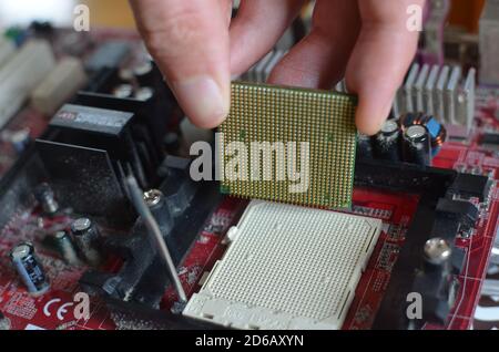 Eine Hand, die eine CPU (Prozessor-Chip) von der Hauptplatine eines alten Computers entfernt. Stockfoto