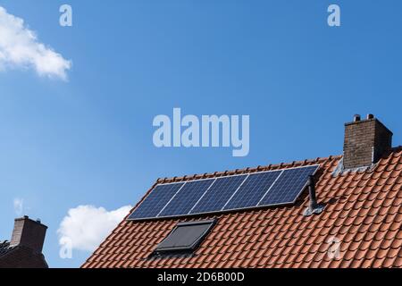 Dach mit roten Dachziegeln, Kamin und Sonnenkollektoren für die Herstellung erneuerbarer Energie und einen klaren blauen Himmel Stockfoto