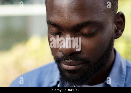 Nahaufnahme Porträt eines ernsten afroamerikanischen Mannes mit geschlossenen Augen. Schöner junger ruhiger Mann in blauem Denim-Hemd auf der Straße Stockfoto