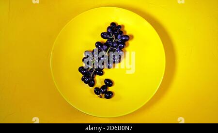 Schwarze Trauben auf einem gelben Teller. Reife Trauben auf gelbem strukturiertem Hintergrund. Konzept: Obst und gesunde Ernährung Stockfoto