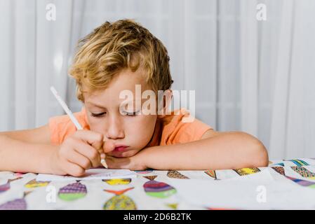 Junger Mann mit gelangweilter Expression beendet seine Hausaufgaben zu Hause, bevor er einschläft. Stockfoto