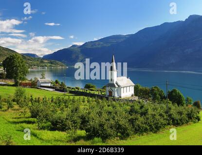 Blick auf Lustrafjord mit EINER weißen Holzkapelle im Vordergrund in Hoyheimsvik an EINEM sonnigen Sommertag mit EINEM Klarer blauer Himmel und EIN paar Wolken Stockfoto