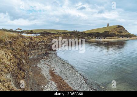 Blick auf Kimmeridge Bay, Dorset UK, Landschaft aussicht auf ruhiges Meerwasser, Steinturm auf dem Hügel mit dramatisch überstrahltem Himmel Stockfoto