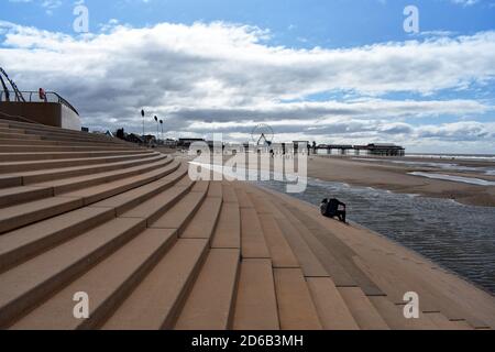 Ein Paar sitzt auf Stufen, die von der Promenade zum Strand in Blackpool, England, führen. Der Central Pier führt in die Irische See. Stockfoto