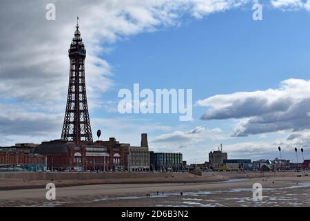 Blick auf den Blackpool Tower und Entertainment Complex vom North Pier. Touristenwanderung am Strand entlang, während die Flut ist. Lancashire, Großbritannien Stockfoto