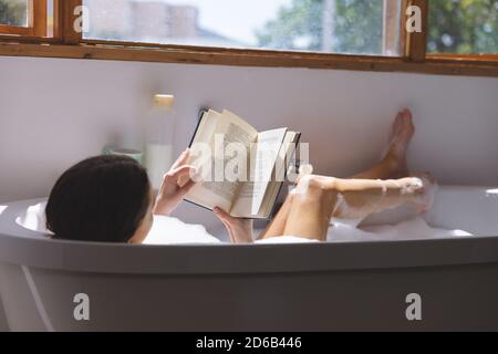 Frau liest Buch, während sie sich in der Badewanne entspannt Stockfoto