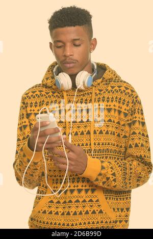 Junger schöner afrikanischer Mann mit Mobiltelefon, während er Kopfhörer trägt Um den Hals Stockfoto