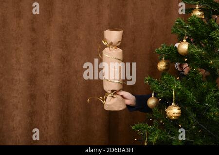 Verlängerte Kinderhand mit einer Neujahrs-Lappen-Überraschung. Von hinten ein beladener Weihnachtsbaum. Stockfoto