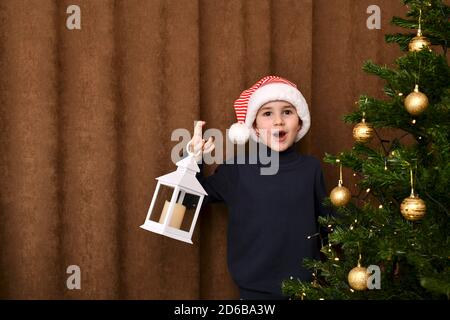 Ein begeistertes Kind sprang hinter dem Weihnachtsbaum mit einer Laterne hervor. Stockfoto