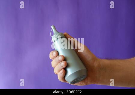 Männliche Hand und graue Plastikflasche mit Sirup. Der Mann hält eine neue Flasche Süßsirup für Eis und Desserts. Selektiver Fokus. Stockfoto