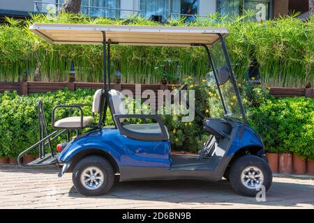 Kleines Golf-Elektroauto in einem Touristenort. Blaues Elektroauto auf dem Straßenrand auf grünem Hintergrund geparkt Stockfoto