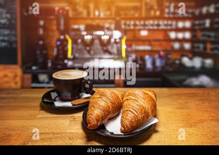 Frisch gebackene Croissants und eine Tasse Kaffee auf einem Holztisch Mit Blur Cafeteria als Hintergrund Stockfoto