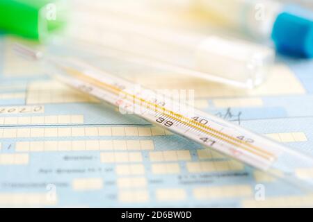 Thermometer auf einem Tisch vor dem Hintergrund eines medizinischen Dokuments. Ein Symptom eines Coronavirus oder einer Grippe Stockfoto