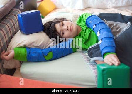 Schöner biracial behinderten kleinen Jungen auf Matratze liegend spielen Mit Schaumstoffblöcken beim Tragen von Armspangen Stockfoto