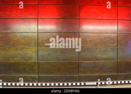 Passagiere, die unter der dramatischen Farbveränderungs-Beleuchtung auf Züge warten Am Bahnhof HafenCity Universität an der U-Bahn Hamburg Stockfoto