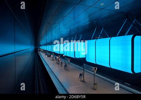 Passagiere, die unter der dramatischen Farbveränderungs-Beleuchtung auf Züge warten Am Bahnhof HafenCity Universität an der U-Bahn Hamburg Stockfoto