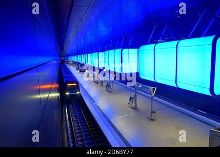 Passagiere, die unter der dramatischen Farbveränderungs-Beleuchtung auf Züge warten Am Bahnhof HafenCity Universität an der U-Bahn Hamburg Stockfoto