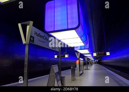 Passagiere, die unter der dramatischen Farbveränderungs-Beleuchtung auf Züge warten Am Bahnhof HafenCity Universität an der U-Bahn Hamburg Stockfoto