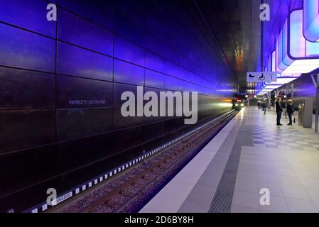 Passagiere, die unter der dramatischen Farbveränderungs-Beleuchtung auf Züge warten Am Bahnhof HafenCity Universität an der U-Bahn Hamburg Stockfoto